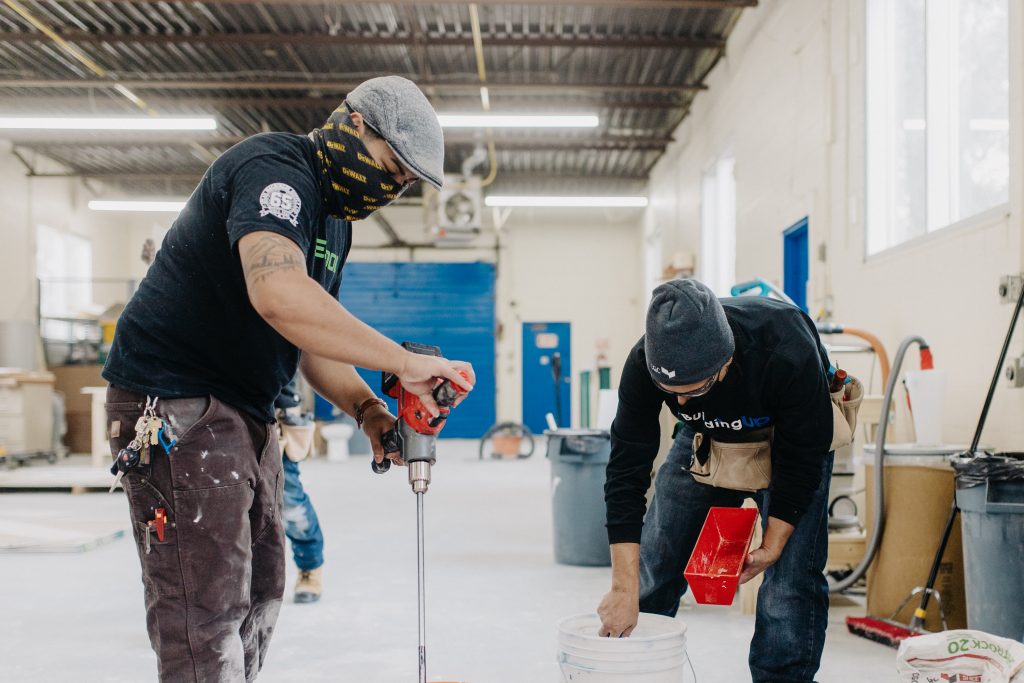 two building up employees work on a construction site wearing masks